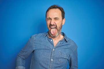 Fototapeta premium Handsome middle age senior man with grey hair over isolated blue background sticking tongue out happy with funny expression. Emotion concept.