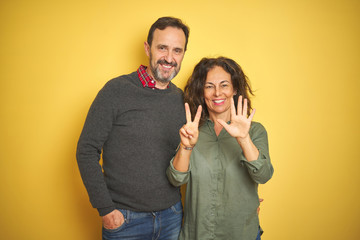 Beautiful middle age couple over isolated yellow background showing and pointing up with fingers number seven while smiling confident and happy.