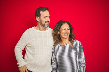 Beautiful middle age couple wearing winter sweater over isolated red background looking away to side with smile on face, natural expression. Laughing confident.