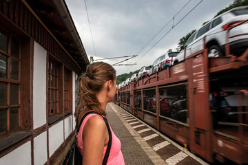 girl standing at the station looks at the freight train carrying cars.