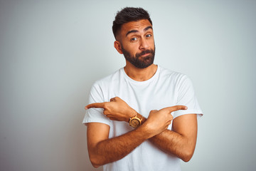 Young indian man wearing t-shirt standing over isolated white background Pointing to both sides with fingers, different direction disagree - obrazy, fototapety, plakaty