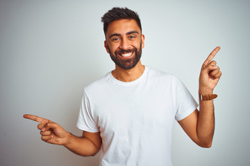 Young indian man wearing t-shirt standing over isolated white background smiling confident pointing with fingers to different directions. Copy space for advertisement
