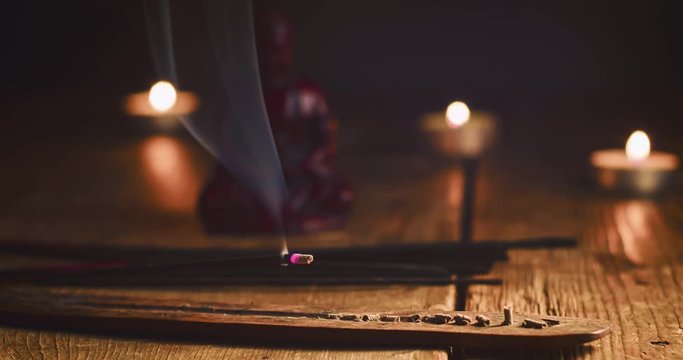 Time lapse of burning incense stick attractively decorated on old rustic wooden planks. Stick holder and Incense stick with smoke on statuette Buddha and burning candles background