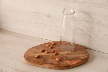Empty glass milk bottle with almonds over wooden board on wooden table, food and health background concept.