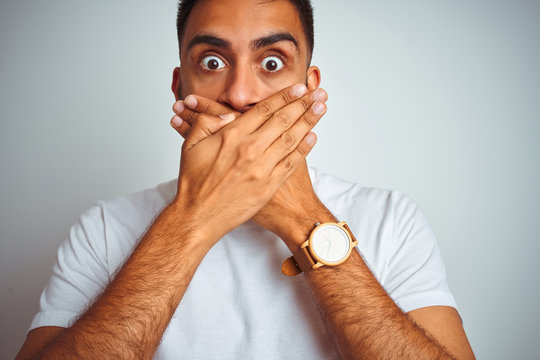 Young indian man wearing t-shirt standing over isolated white background shocked covering mouth with hands for mistake. Secret concept.