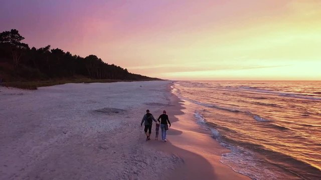Happy Family Enjoying a Walk on a Beach at Sunset. Parents Walking With a Small Child. Sunset Beach Walk Drone Footage. 4k Slowmotion Drone Shot.