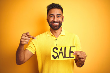 Young arab indian hispanic man holding sale banner over isolated yellow background very happy pointing with hand and finger
