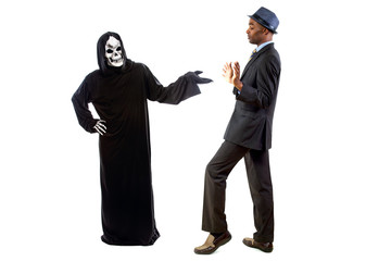Man in a grim reaper halloween ghost costume having fun and scaring a grown businessman in a suit. ...