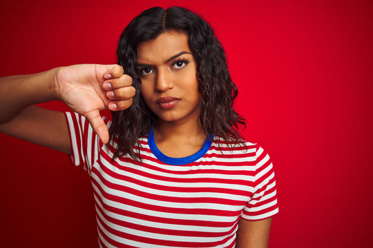 Beautiful transsexual transgender woman wearing stiped t-shirt over isolated red background with angry face, negative sign showing dislike with thumbs down, rejection concept