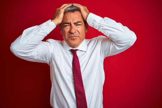 Handsome middle age businessman standing over isolated red background suffering from headache desperate and stressed because pain and migraine. Hands on head.