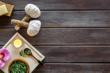 Massage table with thai herbal balls, candles and orchids on dark wooden background top view frame copy space
