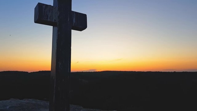 Stone cross on top of a mountain against a sunset. Cross on a sunset background. Stone crem on the mountain at sunset