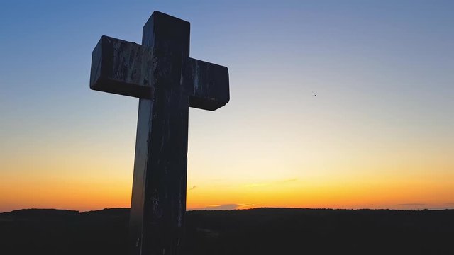 Stone cross on top of a mountain against a sunset. Cross on a sunset background. Stone crem on the mountain at sunset
