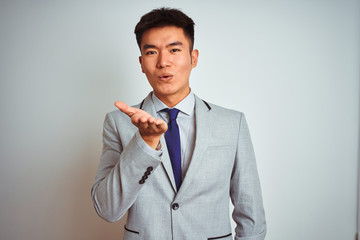 Asian chinese businessman wearing suit and tie standing over isolated yellow background looking at the camera blowing a kiss with hand on air being lovely and sexy. Love expression.