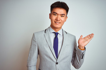 Asian chinese businessman wearing suit and tie standing over isolated white background smiling cheerful presenting and pointing with palm of hand looking at the camera.