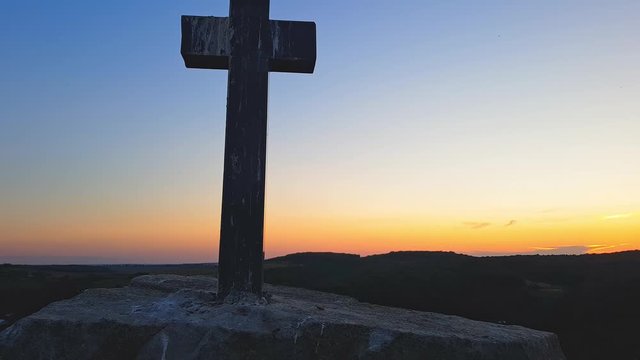 Stone cross on top of a mountain against a sunset. Cross on a sunset background. Stone crem on the mountain at sunset