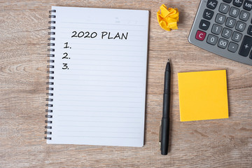 2020 NEW YEAR PLAN word on note with pen and crumbled paper on wooden table background. NEW START, Strategy and Goal concept