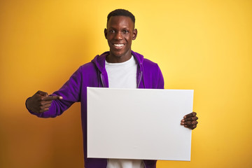 African american man holding banner standing over isolated yellow background very happy pointing with hand and finger