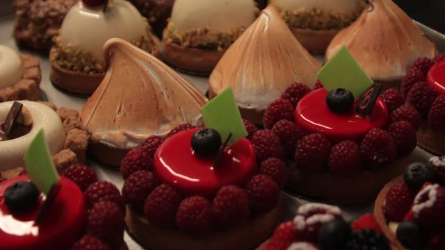 Ornate vibrant pastry baked goods treats on display in a fine patisserie handheld shot