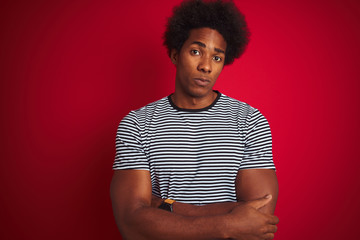 Fototapeta na wymiar Young american man with afro hair wearing navy striped t-shirt over isolated red background skeptic and nervous, disapproving expression on face with crossed arms. Negative person.
