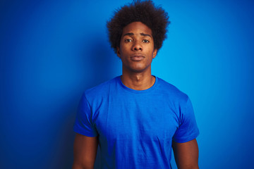 Fototapeta na wymiar African american man with afro hair wearing t-shirt standing over isolated blue background with serious expression on face. Simple and natural looking at the camera.