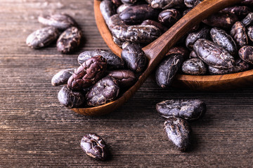 Whole dry cocoa beans, powder in wooden bowls spoon on old rustic background.