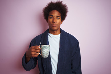 Afro american man wearing pajama drinking coffee standing over isolated pink background with a...