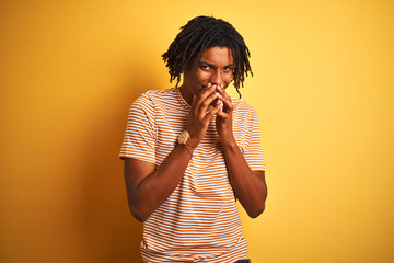 Afro man with dreadlocks wearing striped t-shirt standing over isolated yellow background laughing...