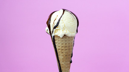 Chocolate sauce on Vanilla ice cream scooped in waffle cone on pink background, Closeup Front view Food concept.