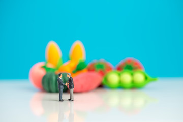 Miniature toys studio set up - two businessman shakes hand in agreement concept with fresh produce in the background.