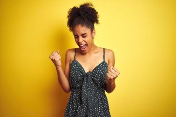African american woman wearing summer casual green dress over isolated yellow background very happy and excited doing winner gesture with arms raised, smiling and screaming for success. 