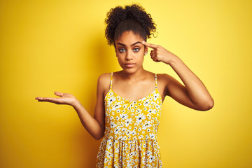 African american woman wearing casual floral dress standing over isolated yellow background...