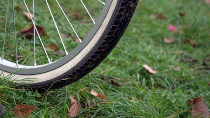 Close-up of part of the wheel. The wheel stands on the green grass and brown fallen leaves lie. The concept of Cycling in autumn on a bike is good for health