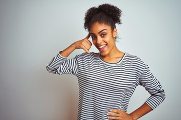 Fototapeta premium African american woman wearing navy striped t-shirt standing over isolated white background smiling doing phone gesture with hand and fingers like talking on the telephone. Communicating concepts.