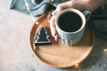 Women's hand hold a cup of coffee on beige background. Winter holiday, cozy mood christmas concept. Copy space