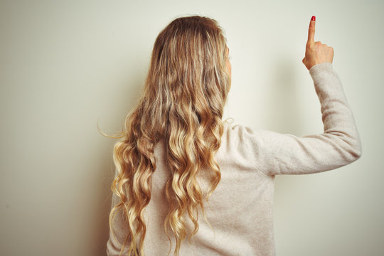 Beautiful woman wearing winter turtleneck sweater over isolated white background Posing backwards pointing ahead with finger hand