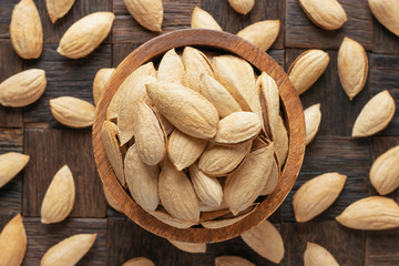 shelled paper almonds nuts in wooden bowl, top view.