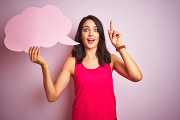 Beautiful woman holding speech bubble over pink isolated background surprised with an idea or...