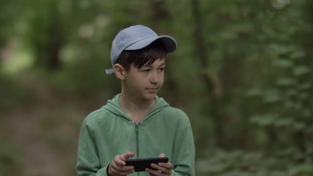 boy walking in the forest and uses a phone outdoors have fun