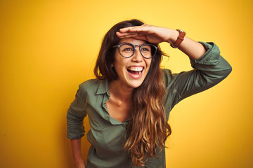 Young beautiful woman wearing green shirt and glasses over yelllow isolated background very happy...