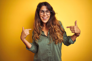 Young beautiful woman wearing green shirt and glasses over yelllow isolated background looking...