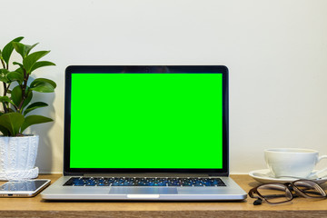 Laptop computer with blank green screen with smart phone, spectacles and a coffee cup on brick wall on wooden table interior of room room hotel background,Work business in leisure with travel holiday