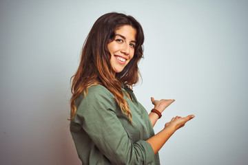 Young beautiful woman wearing green shirt standing over grey isolated background Inviting to enter smiling natural with open hand