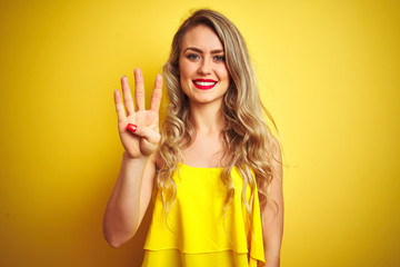 Young attactive woman wearing t-shirt standing over yellow isolated background showing and pointing up with fingers number four while smiling confident and happy.