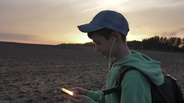 funny boy with backpack walks outdoors at sunset and uses the phone, listening to music, travel concept