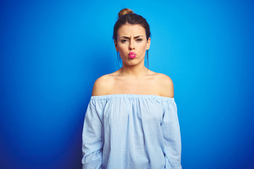Fototapeta na wymiar Young beautiful woman wearing bun hairstyle over blue isolated background puffing cheeks with funny face. Mouth inflated with air, crazy expression.