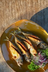 Fired fish with vegetables in dish on wooden table, free space for text.