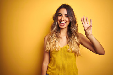 Young beautiful woman wearing t-shirt over yellow isolated background showing and pointing up with fingers number four while smiling confident and happy.