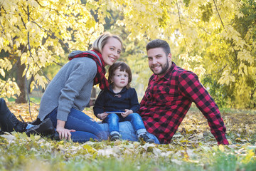 Fototapeta premium Happy family mother father and baby in autumn park playing with leaves.