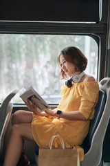 Young woman reading book while moving in the modern tram, happy passenger at the public transport